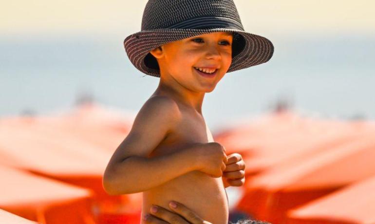 Bambino felice in spiaggia con cappello e costume.