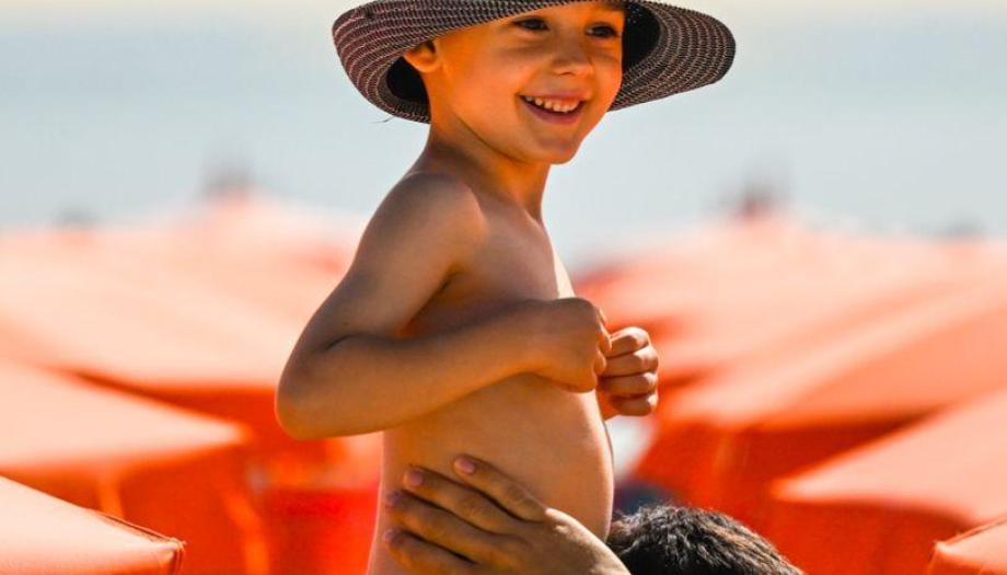 Bambino felice in spiaggia con cappello e costume.