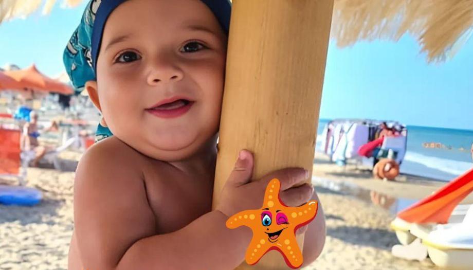 Bambino sorridente in spiaggia con cappello blu.