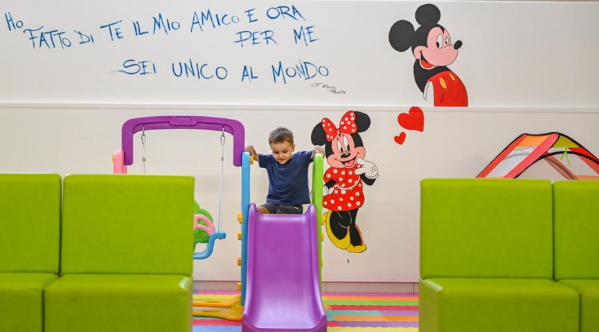 Bambino gioca su scivolo colorato, parete decorata con personaggi Disney.