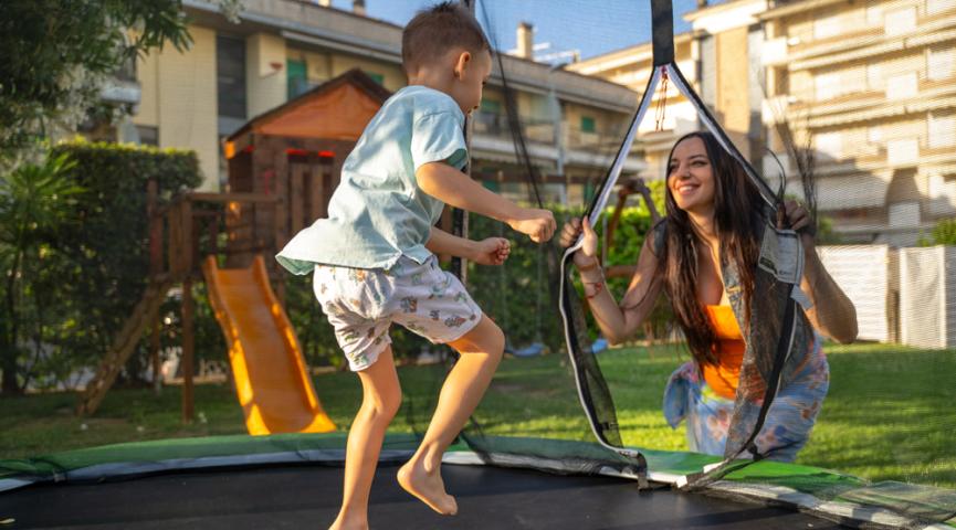 Bambino e donna giocano su un trampolino in giardino.