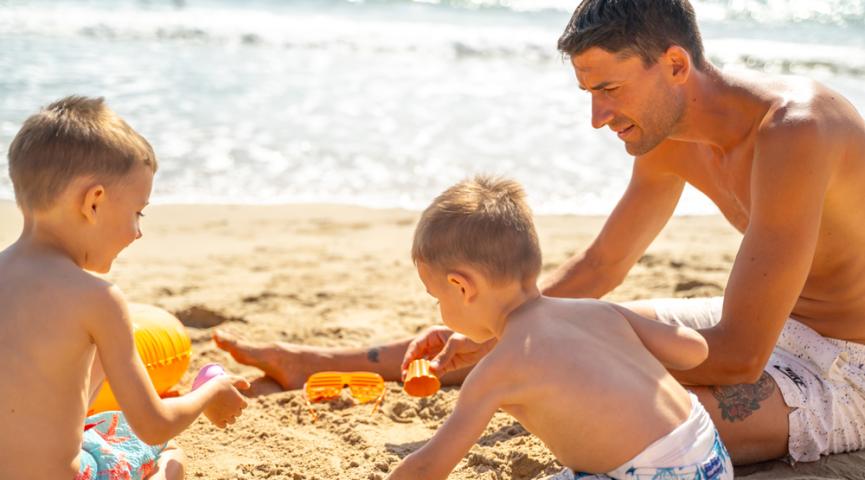 Papà e figli giocano sulla spiaggia con la sabbia.