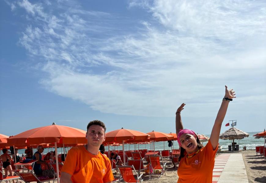 Due persone felici in spiaggia con ombrelloni arancioni.