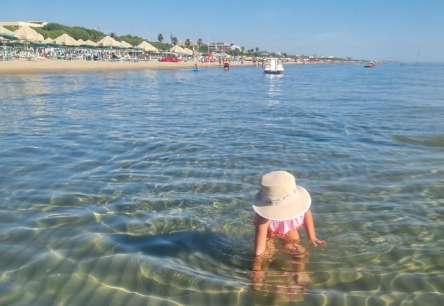 Bambina gioca in acqua limpida sotto il sole estivo.