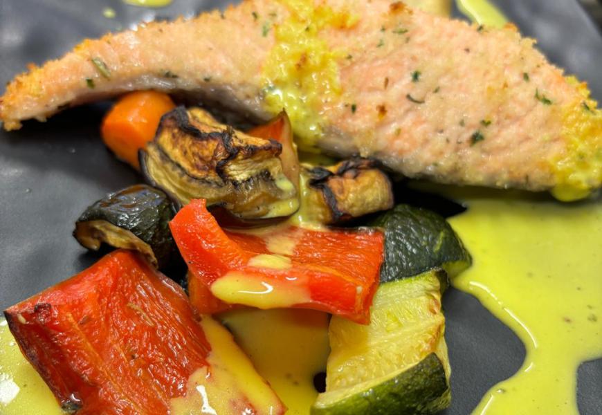 Salmone con verdure grigliate e salsa cremosa su piatto nero.