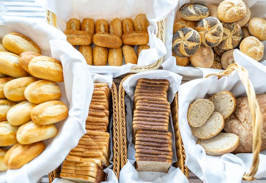 Varietà di pane in ceste di vimini con tovaglioli bianchi.