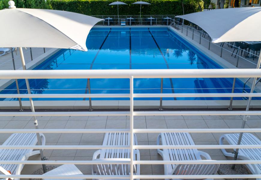 Piscina all'aperto con lettini e ombrelloni bianchi.