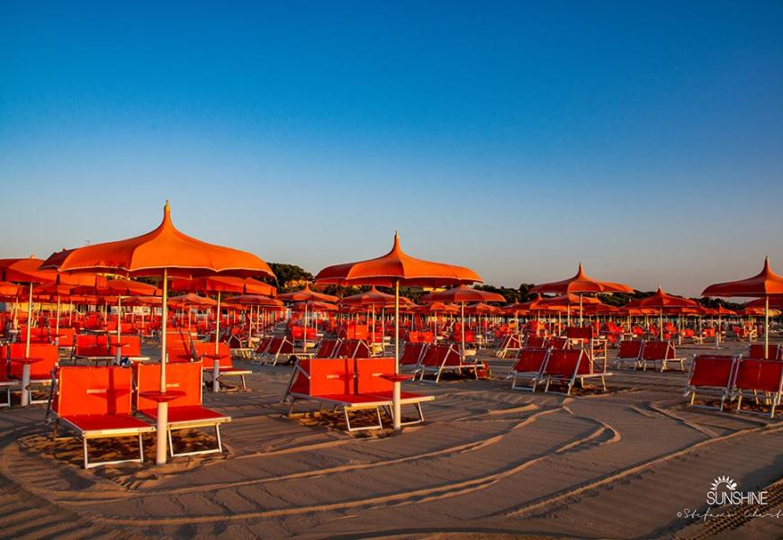 Spiaggia con ombrelloni arancioni al tramonto, atmosfera tranquilla.