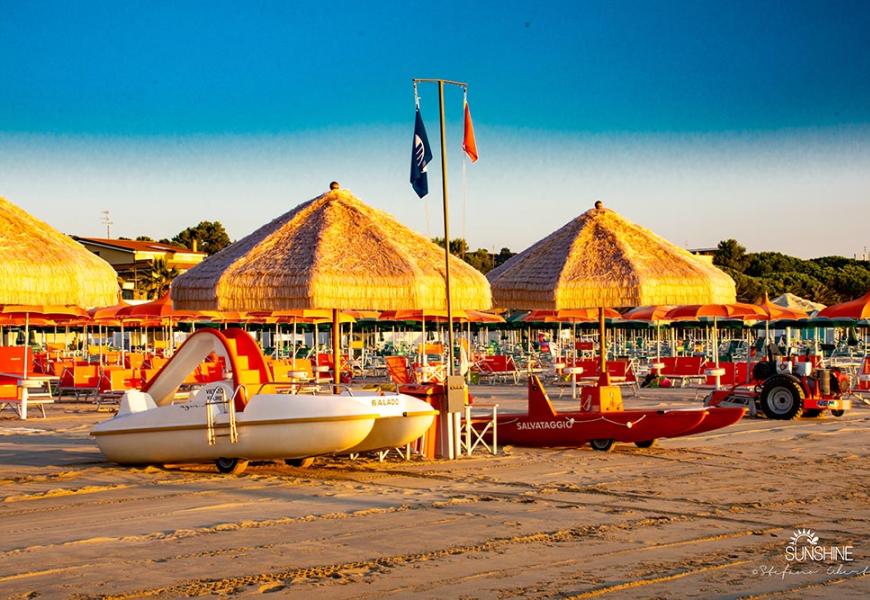 Spiaggia con ombrelloni di paglia e pedalò al tramonto.