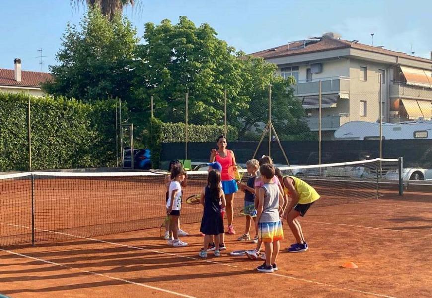 Bambini giocano a tennis con un istruttore su un campo all'aperto.