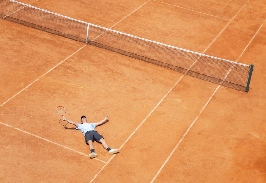 Giocatore steso su campo da tennis in terra battuta.