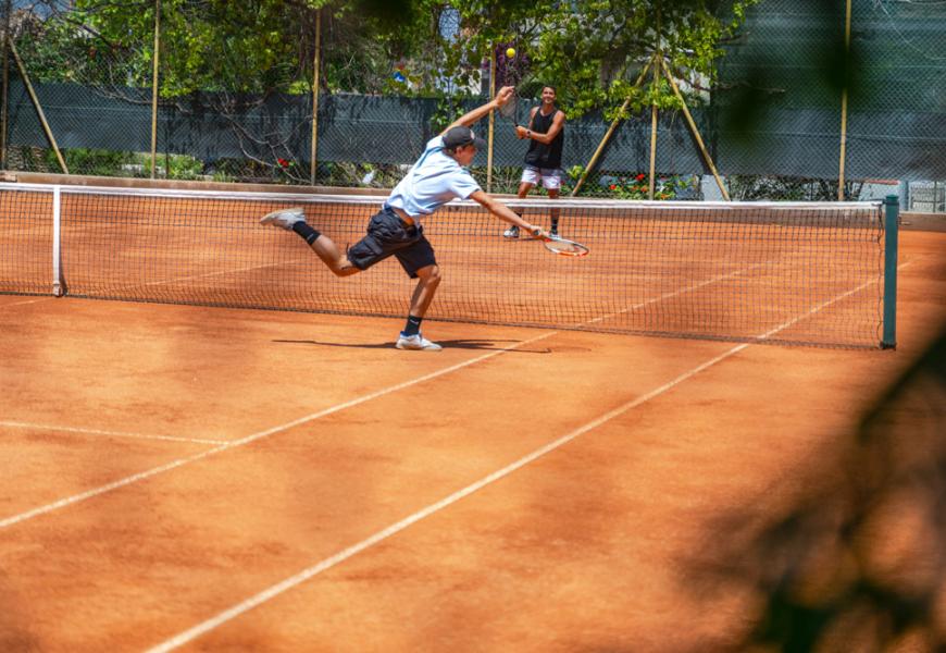 Partita di tennis su campo in terra battuta, giocatori in azione.