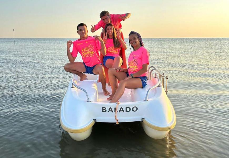 Quattro persone su un pedalò al tramonto, indossano magliette rosa.