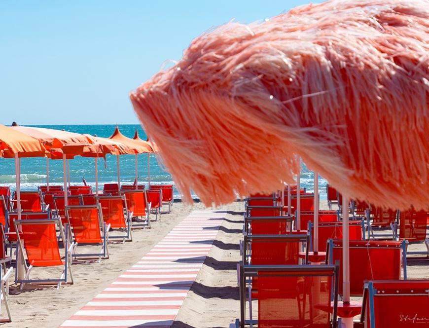 Ombrelloni arancioni allineati su una spiaggia sabbiosa.